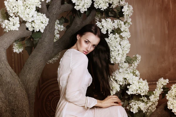 Porträt einer attraktiven Frau sitzt im Blumenbaum und blickt in die Kamera — Stockfoto