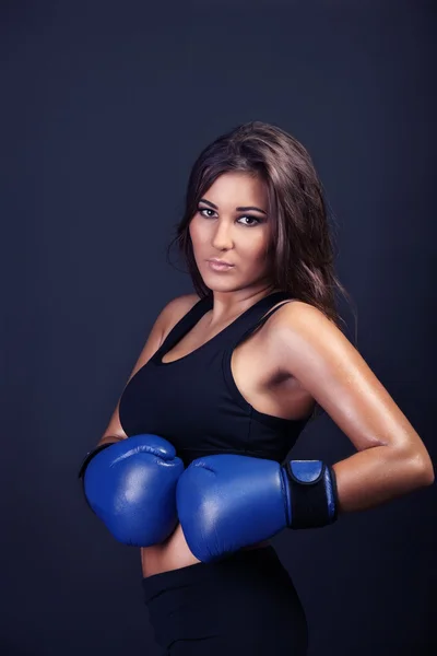 onun mavi boks kollarını yanında beline tutarak ve kameraya bakarak eldiven giymiş sportif kadın boksör Studio portresi