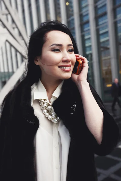 Magabiztos ázsiai üzletasszony mosollyal az arcán, Londonban az utca, a város állt, és beszélt a mobiltelefon Stock Kép