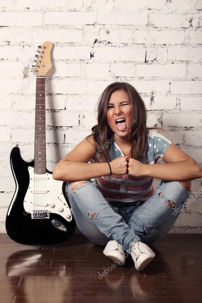 Young female musician is making silly faces sitting on the floor near to her guitar