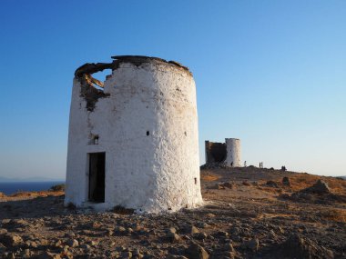 Mavi denizin ve yaz gökyüzünün arka planına karşı, bir dağ pelerinindeki eski, harap değirmenler.