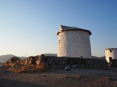 Mavi denizin ve yaz gökyüzünün arka planına karşı, bir dağ pelerinindeki eski, harap değirmenler.