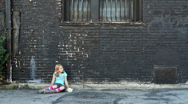 Girl sitting on ground next to brick wall — Stock Photo, Image