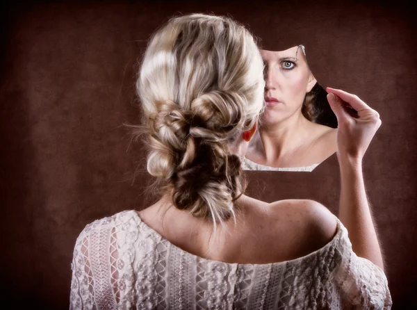 Woman looking into a broken mirror Stock Picture