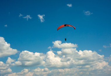 Mavi gökyüzünde bulutların arka planında uçan kırmızı paraglider. Güneşli bir günde gökyüzünde paraşütle atlamak.