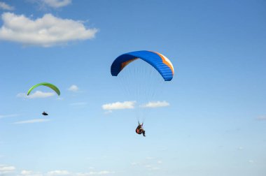 İki paraşütler bulutlar arka planı mavi gökyüzünde uçan. Güneşli bir havada yamaç paraşütü.