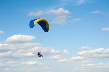 Tek başına mavi ve sarı paraglider bulutların arkasında mavi gökyüzünde uçuyor. Güneşli bir günde gökyüzünde paraşütle atlamak.