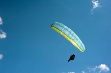 Tek başına mavi ve sarı paraglider bulutların arkasında mavi gökyüzünde uçuyor. Güneşli bir günde gökyüzünde paraşütle atlamak.