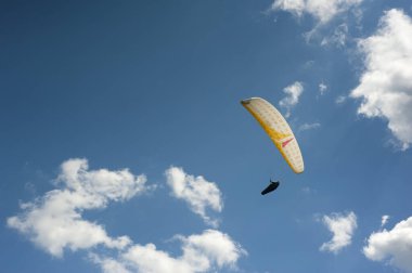 Bulutların arkasında mavi gökyüzünde uçan tek başına beyaz bir paraglider. Güneşli bir günde gökyüzünde paraşütle atlamak.