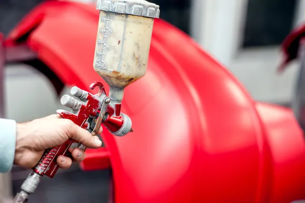 Nahaufnahme einer Spritzpistole mit roter Farbe, die ein Auto bemalt — Stockfoto