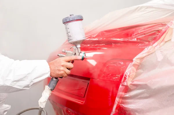 Auto pintor pulverizando tinta vermelha no carro na oficina de automóveis — Fotografia de Stock