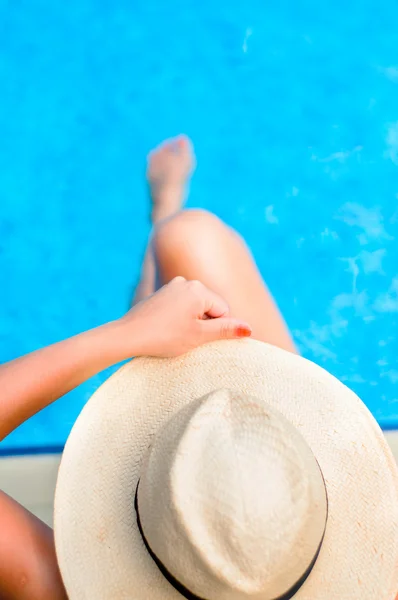 Mujer joven disfrutando del sol en la piscina mientras sostiene un sombrero — Foto de Stock