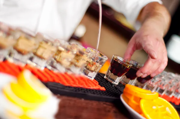 Bartender pours alcoholic drink into small glasses on bar — Stock Photo, Image