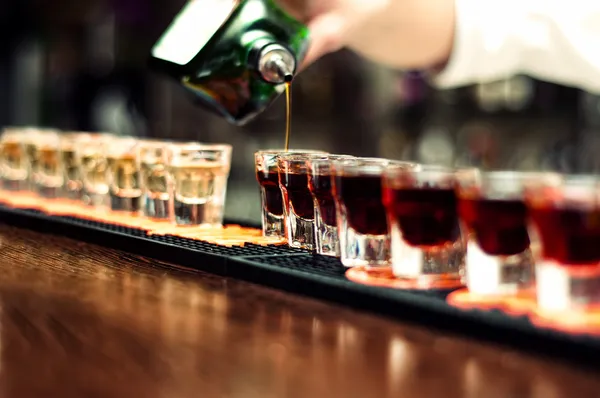 Barman nalije alkoholický nápoj do malých sklenic na baru — Stock fotografie