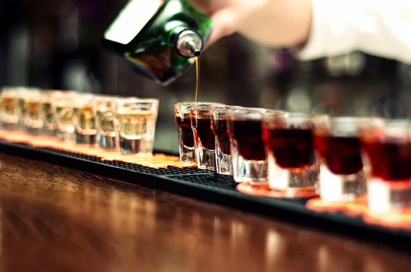 Bartender pours alcoholic drink into small glasses on bar — Stock Photo, Image