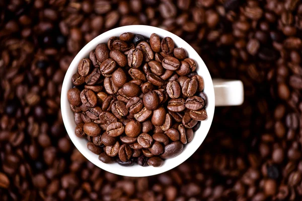 Koffiemok gevuld met koffiebonen en koffie achtergrond — Stockfoto