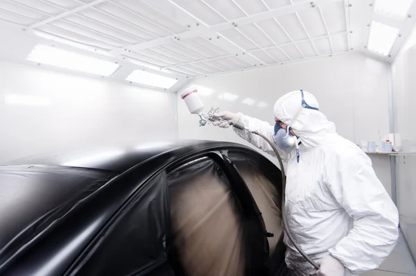 Automotive mechanical engineer painting the body of a black car