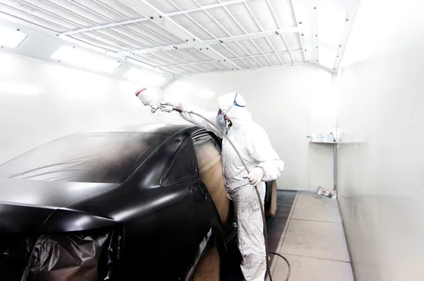 Automobilindustrie - Ingenieur lackiert und arbeitet an einer schwarzen Karosserie eines Autos und trägt Schutzausrüstung — Stockfoto