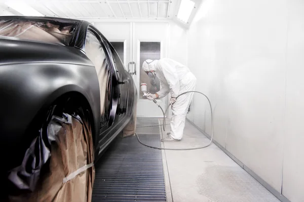 Trabajador pintando un coche negro en un garaje especial, con un traje blanco —  Fotos de Stock