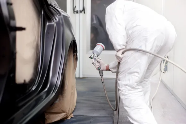 Ingeniero de vehículos trabajando y rociando pintura negra en un coche en taller de carrocería — Foto de Stock