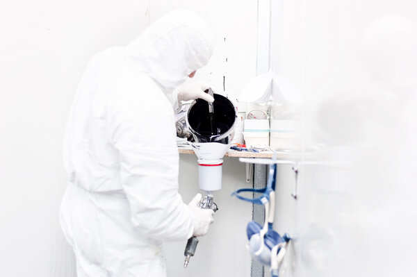 Авторабочий готовит черную краску для кузова автомобиля в белом специальном костюме
