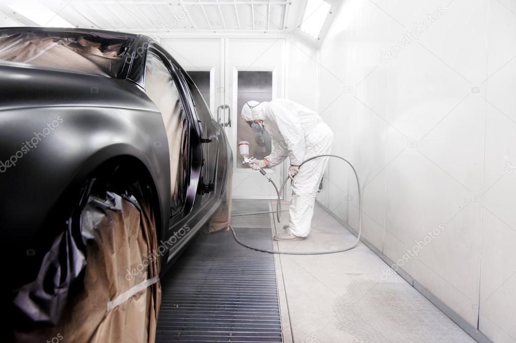 Worker painting a black car in a special garage, wearing a white costume