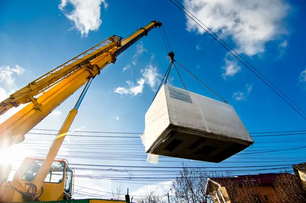 Industrial Crane operando y levantando un generador eléctrico contra la luz solar y el cielo azul Imagen De Stock