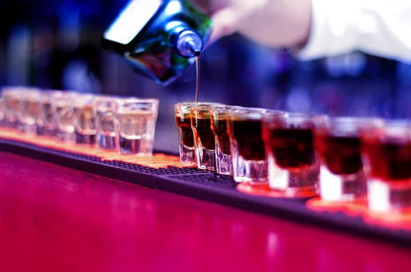 Bartender pouring strong alcoholic drink into small glasses on bar, shots — Stock Photo, Image