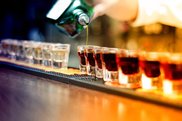 Bartender pouring strong alcoholic drink into small glasses on bar, shot glasses — Stock Photo, Image