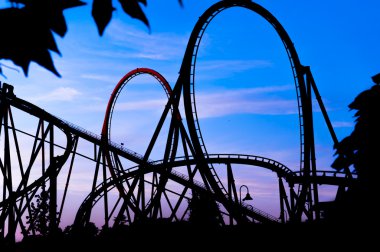 mavi bir gün batımı sırasında lunaparkta entartaiment tematik park adlı bir roller coaster silüeti