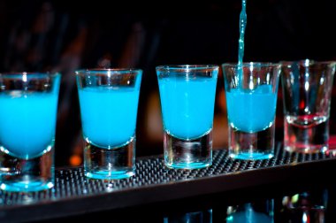Barmen dökülen küçük gözlük içine mavi alkollü içki siyah arka plan üzerinde bar