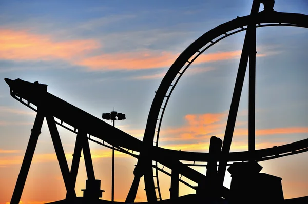 Silueta de puesta de sol de una montaña rusa en un parque de atracciones temático —  Fotos de Stock