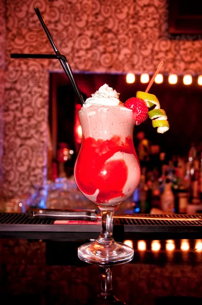 Sweet mix of candy syrops in a long cocktail with whipped cream and strawberry, served in a glass on bar with straws — Stock Photo, Image
