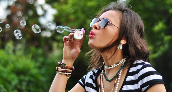 Portrait of an attractive brunette blowing bubbles in the park — Stock Photo, Image