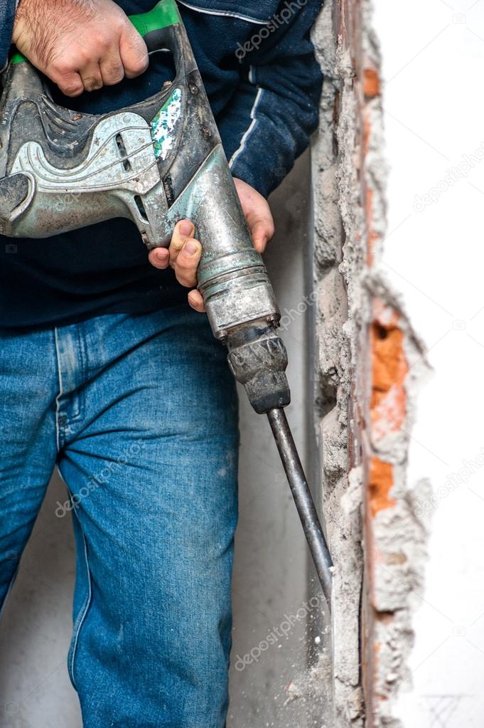 Professional worker handling an jackhammer and drilling into interior