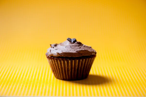 Ein hausgemachter Schokoladen-Cupcake mit braunem Schokoladeneis-Belag isoliert auf gelb — Stockfoto