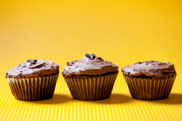 Three chocolate velvet cupcakes with dark chocolate ice cream topping isolated on yellow — Stock Photo, Image