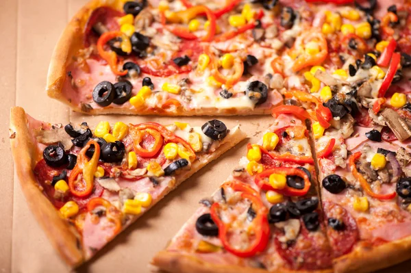 Włoska pizza zbliżenie z wyciąć kawałek. Pizza z szynka, pepperoni, oliwki, kukurydza i papryki — Zdjęcie stockowe