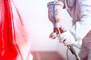 Close-up of spray gun with red paint painting a car in special booth clipart