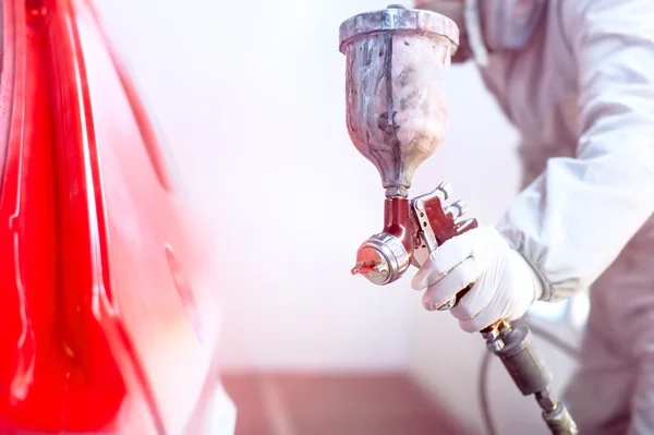 Primer plano de pistola con pintura roja pintando un coche en cabina especial —  Fotos de Stock