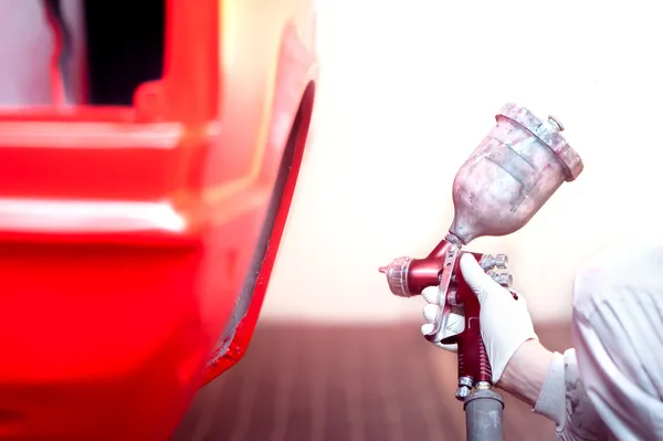 Worker painting a red car or element in a special garage, wearing a white costume — Stock Photo, Image