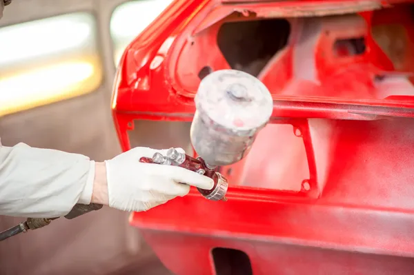 Nahaufnahme einer Lackierpistole, die ein rotes Auto in einer Lackierkabine bemalt — Stockfoto