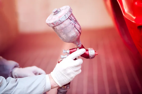 Arbetstagaren målning en röd bil i paiting monter med professionella verktyg och sprutpistol Stockbild