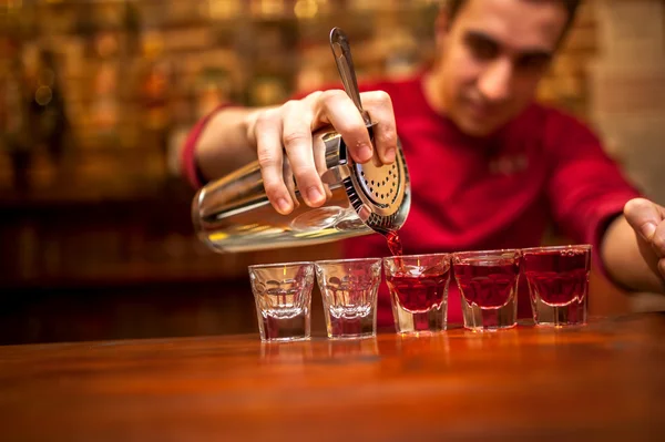 Barman with cocktail shaker pouring red alcoholic drink into glasses in bar — Stock Photo, Image