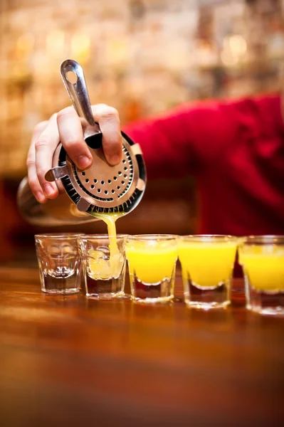 Cantinero vertiendo fuerte bebida alcohólica en vasos pequeños en el bar — Foto de Stock