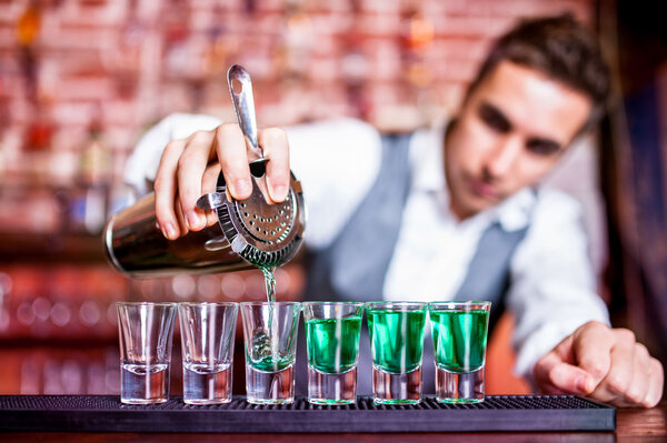 Bartender pouring blue curacao alcoholic cocktail in glasses on bar
