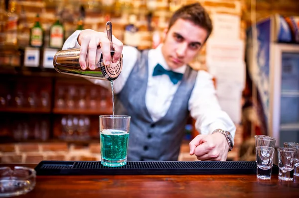 barman pouring a cocktail drink and looking at camera