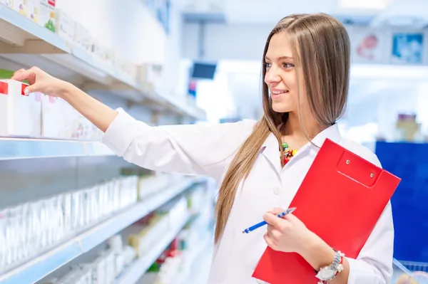 Blonde apotheker plukken van geneeskunde en geneesmiddelen uit planken — Stockfoto