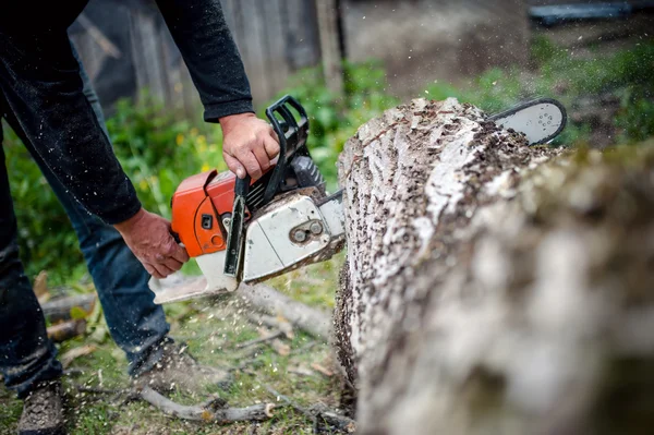 Mann mit benzinbetriebener Motorsäge schneidet Feuerholz von Bäumen im Wald oder Garten — Stockfoto