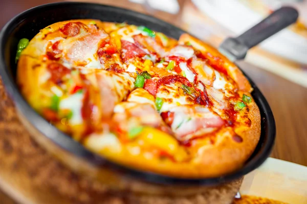 Close-up van hete pizza met verse ingrediënten en groenten geserveerd op de hete plaat. pizza met ham, spekjes en paprika 's — Stockfoto